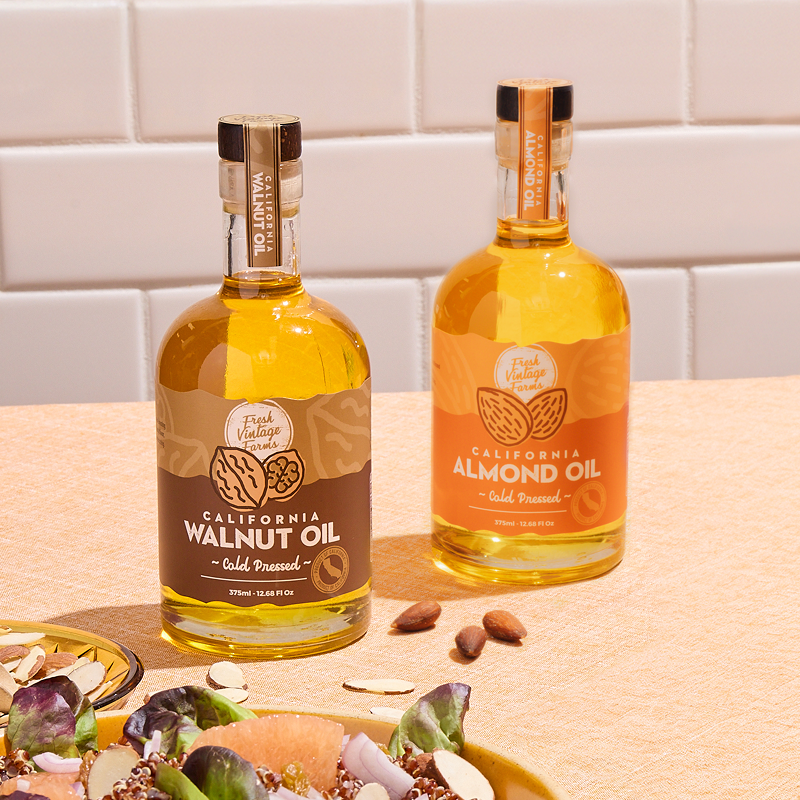 Two bottles of California Walnut Oil and Almond Oil on a wooden surface with a tiled wall background.